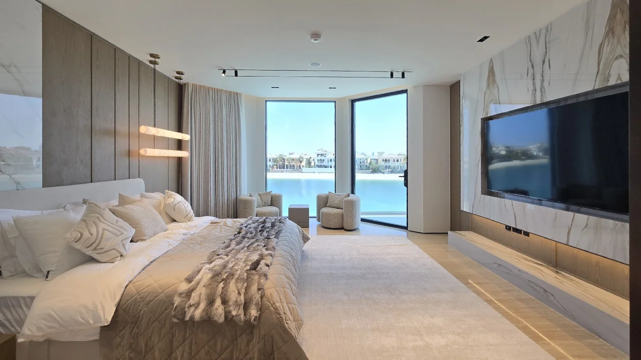 Master Bedroom After Renovation with Waterfront View Renovated Palm Jumeirah master bedroom with floor-to-ceiling waterfront windows, upholstered bed, marble-look TV wall and window seating