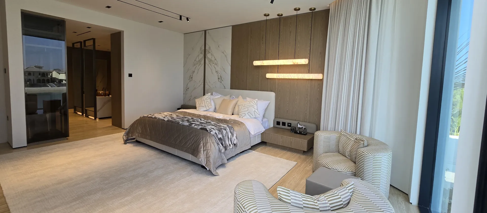 Palm Jumeirah Master Bedroom Before and After Palm Jumeirah master bedroom after full renovation with waterfront glazing, timber headboard wall, lounge chairs and dressing area