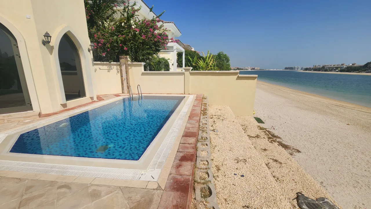 Palm Jumeirah Garden Home swimming pool before remodeling with dark blue mosaic, ladder access, mixed border tiles and beach-side wall