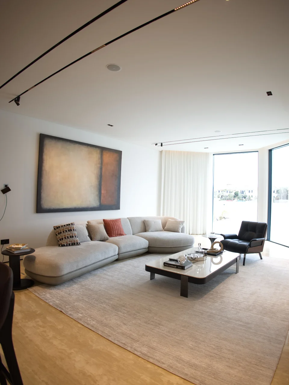 Soft contemporary Palm Jumeirah living room with cream sectional sofa, abstract wall art, black leather lounge chair, pale rug, and waterfront corner view