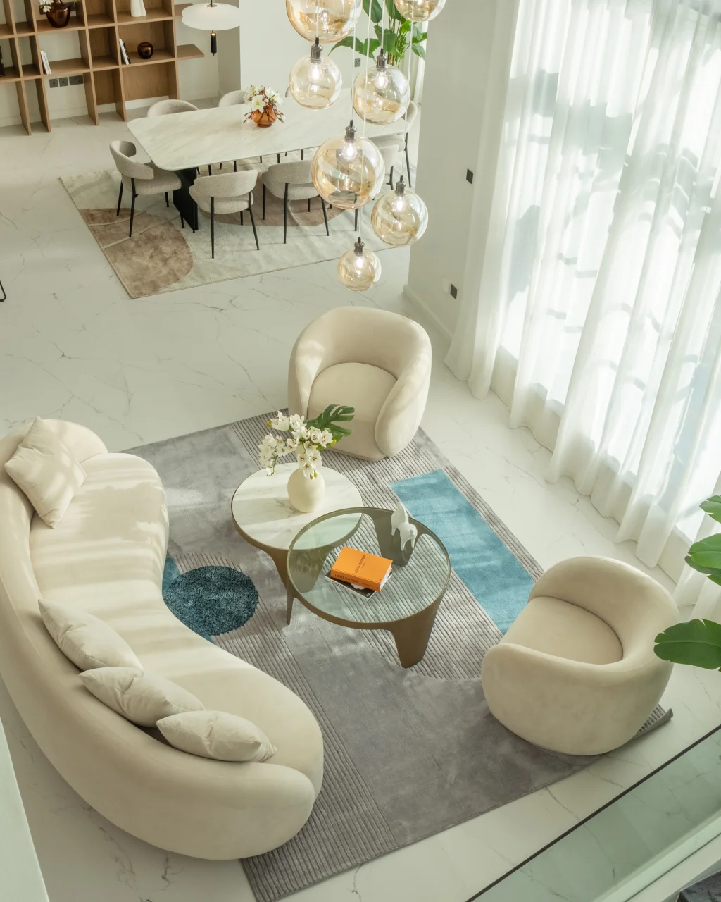 Top view of Jumeirah Islands lounge with curved cream sofa, round armchairs, bubble pendants, glass coffee table, blue accent rug, and dining area