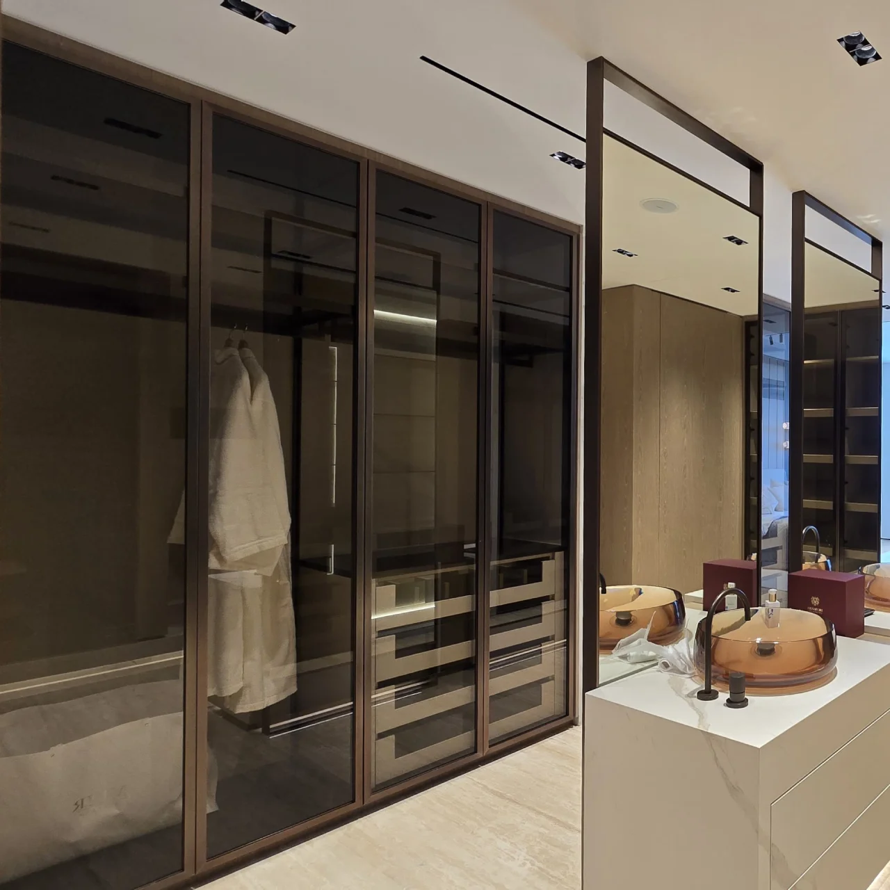 دولاب ملابس walk-in مع خزائن زجاجية مدخنة، جزيرة تسريحة مزدوجة، أحواض كهرمانية، روب معلق، أدراج واتصال بالحمام الرئيسي.