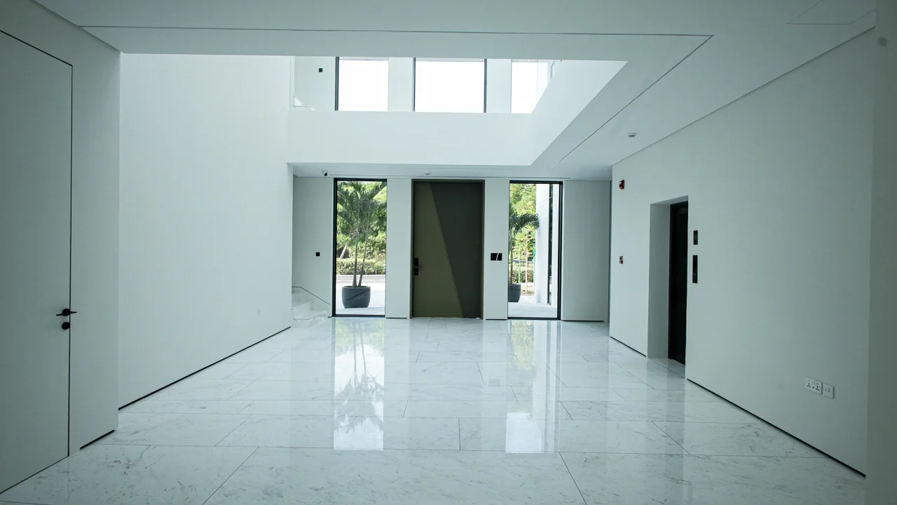 Double-height entrance hall of Casa Azul villa with white marble-effect flooring, main door, tall glazing and passenger lift