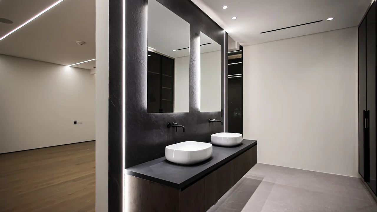 Master-suite vanity area with two vessel basins, wall-mounted black taps, illuminated mirrors and direct connection to the bedroom