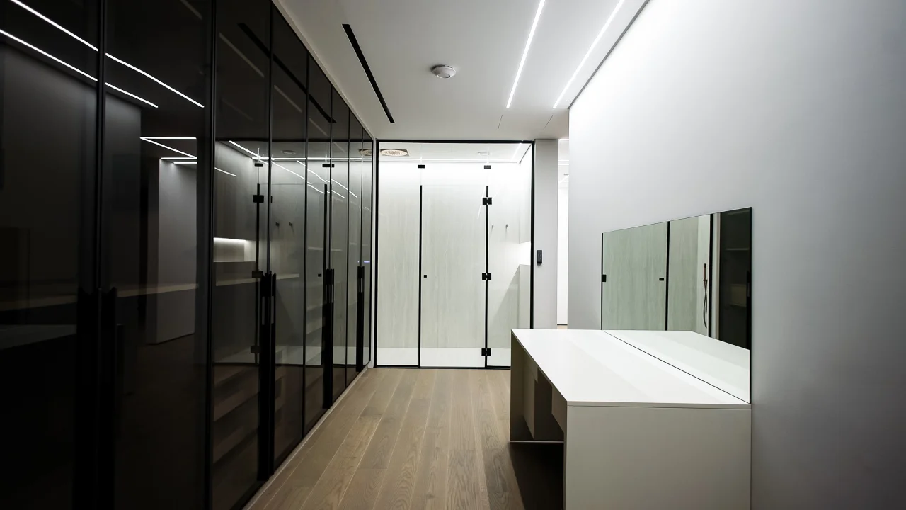 Walk-in wardrobe with smoked-glass cabinets, black metal framing, timber flooring and a central white storage island