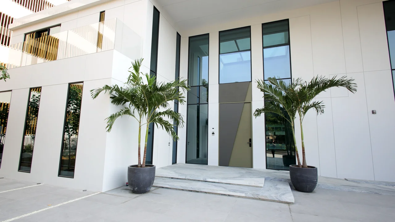 Main entrance of Casa Azul with double-height glazing, oversized entrance door, white exterior panels and two potted palms