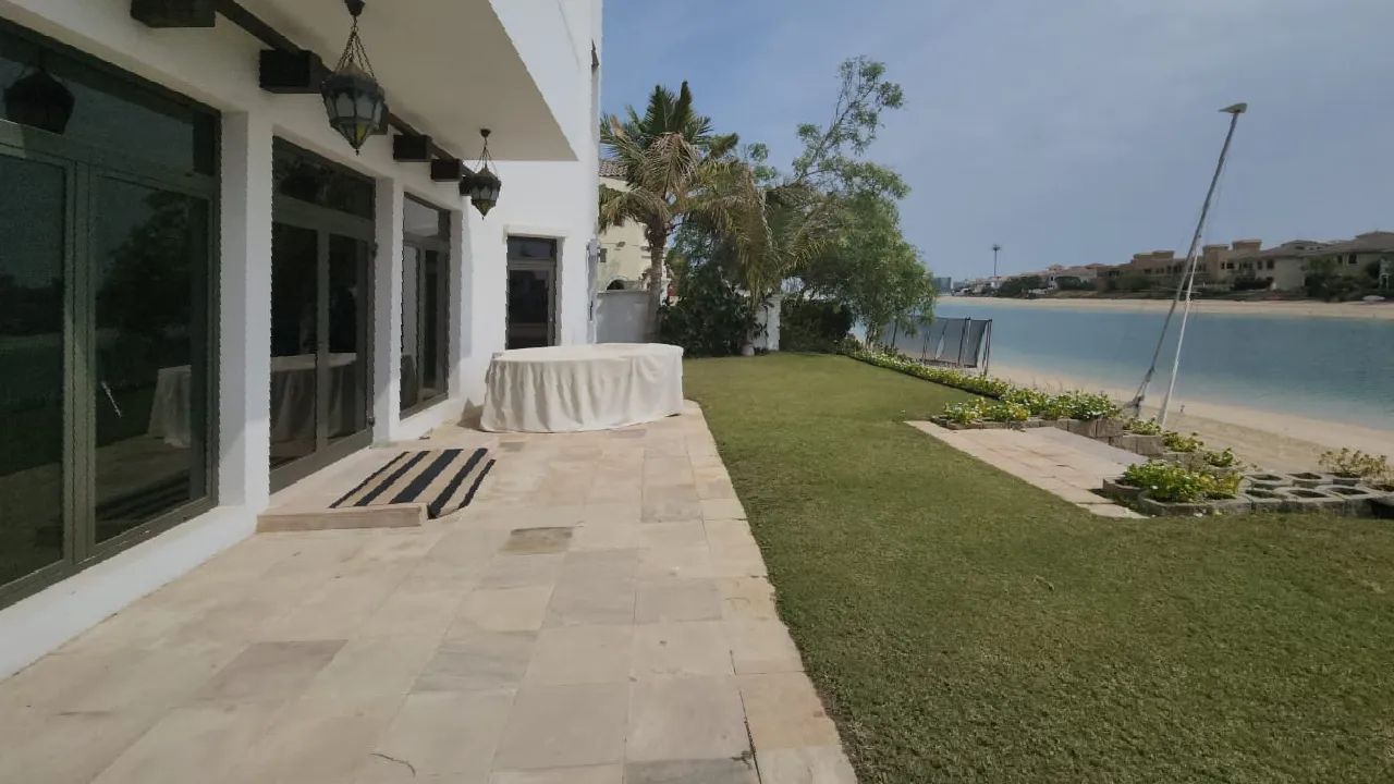 Original waterfront lawn and beige stone terrace before new swimming pool construction at Palm Jumeirah Garden Home