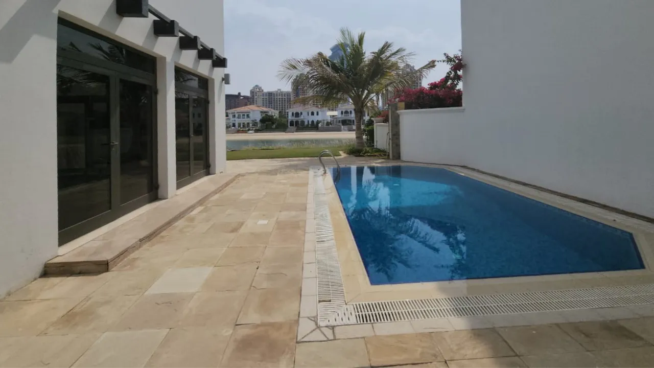 Original dark blue rectangular side swimming pool with beige stone paving before Palm Jumeirah villa renovation