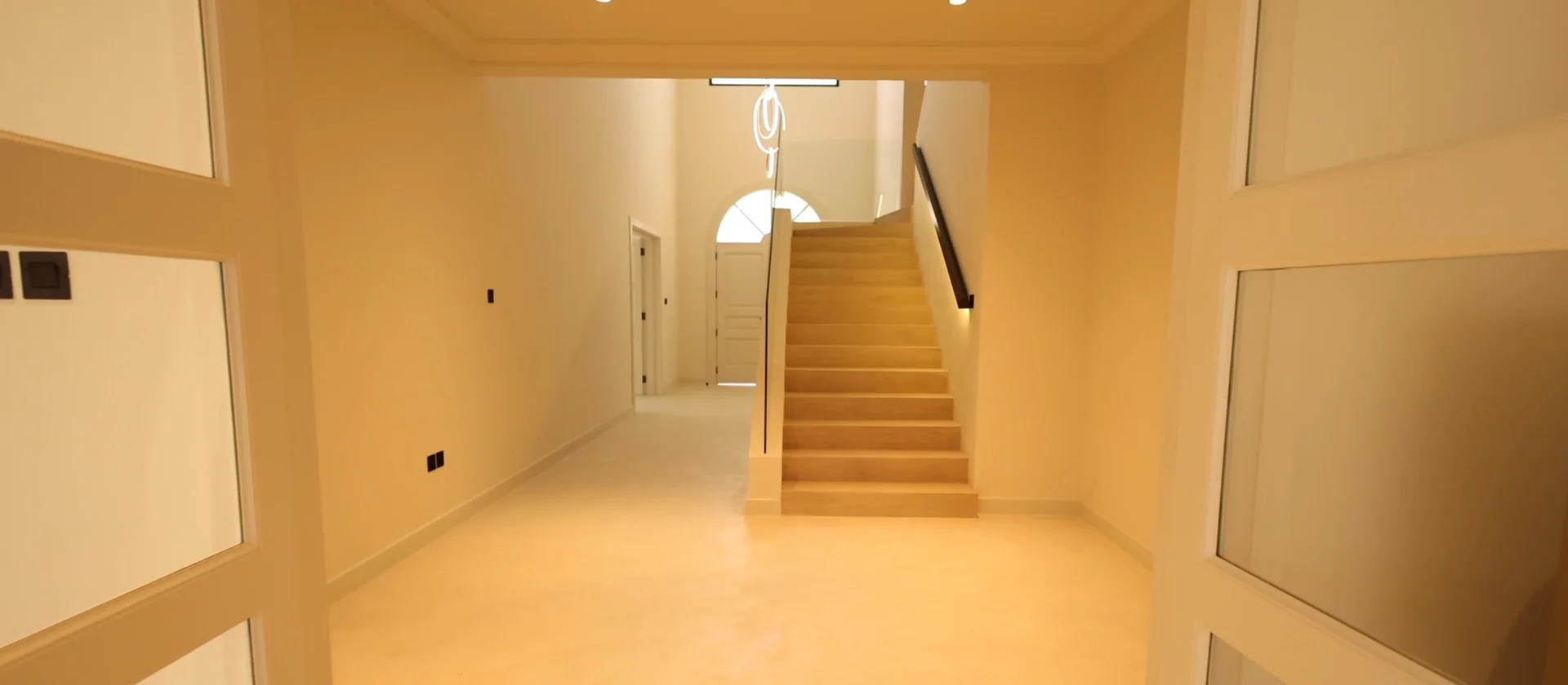 Renovated Palm Jumeirah Garden Home entrance hall with sandy microcement floor, staircase, glass balustrade and integrated handrail lighting