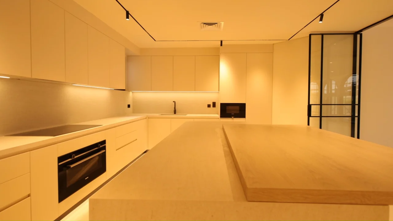 Renovated Palm Jumeirah villa kitchen with cream full-height cabinetry, stone island, raised timber counter, integrated appliances and black track lighting
