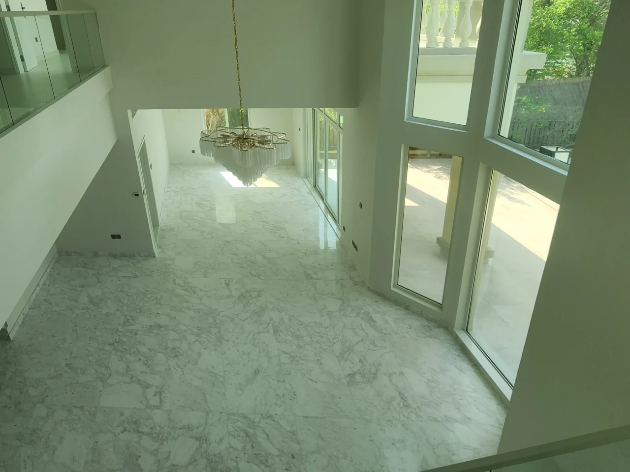 Top view of Jumeirah Islands villa hall before renovation showing a large open floor area, tall glazing and glass balustrades
