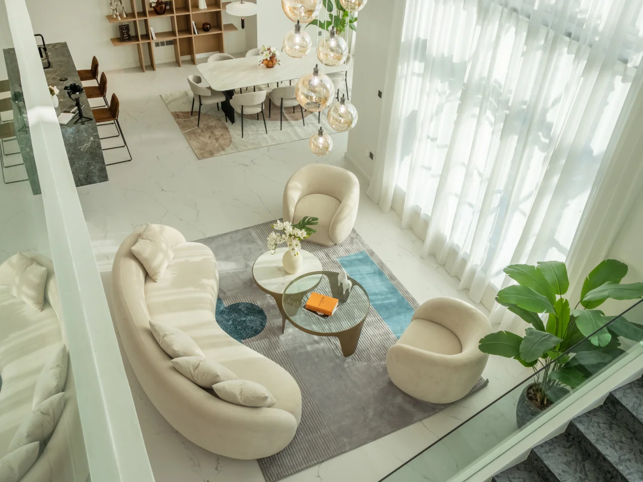 Jumeirah Islands double-height living room after renovation from upper floor Top view of renovated Jumeirah Islands double-height living room with curved seating, dining area, rug and full-height curtains