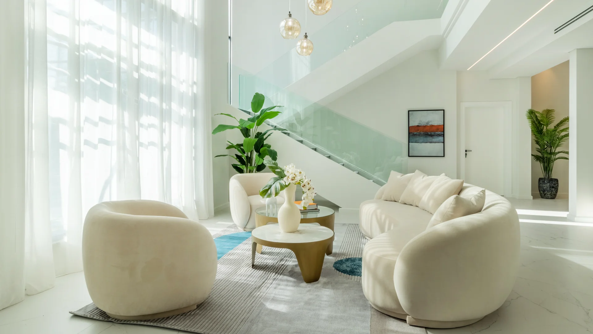 Completed Jumeirah Islands villa living room and staircase Completed Jumeirah Islands villa living room with curved cream seating, full-height sheer curtains, glass balustrade and dark stone staircase
