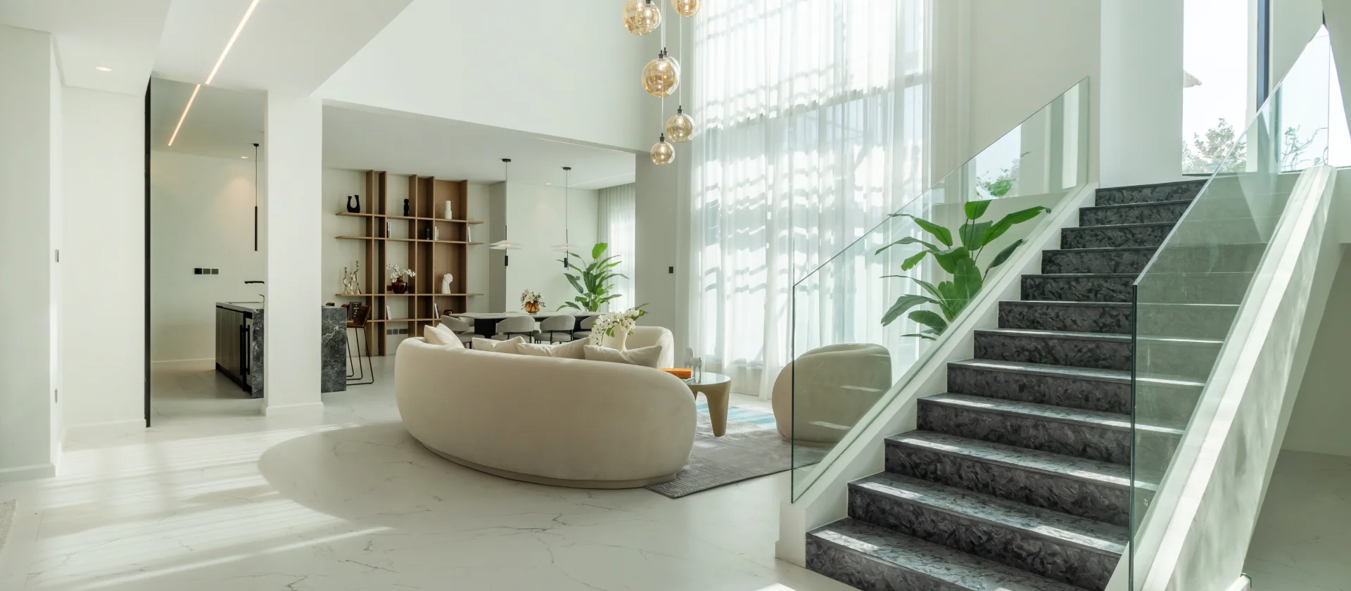 Jumeirah Islands villa hall and living room after renovation Renovated double-height villa hall and living room in Jumeirah Islands Dubai with curved seating and dark stone staircase