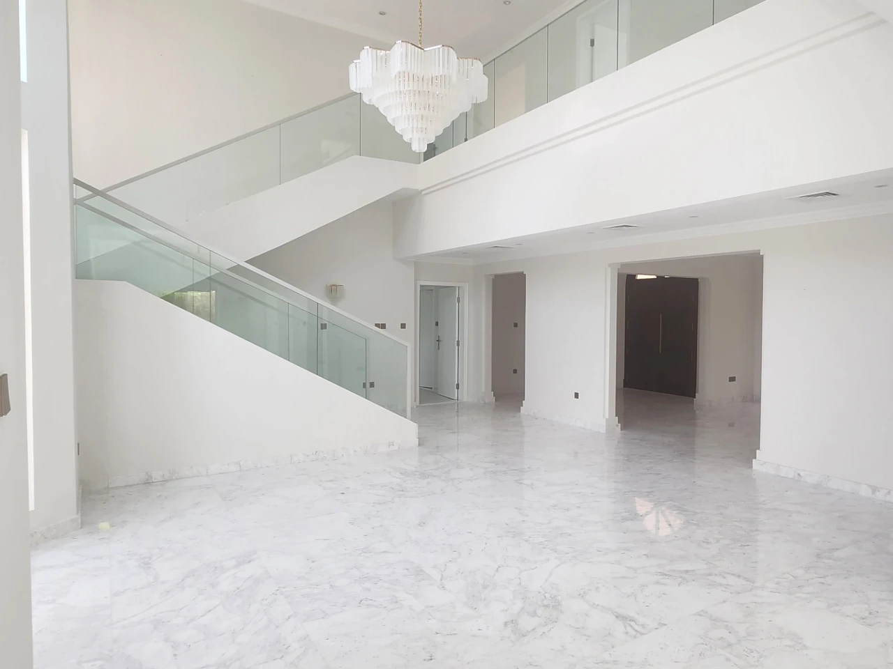 Jumeirah Islands double-height villa hall before renovation with open marble-effect floor, glass staircase and minimal furnishing