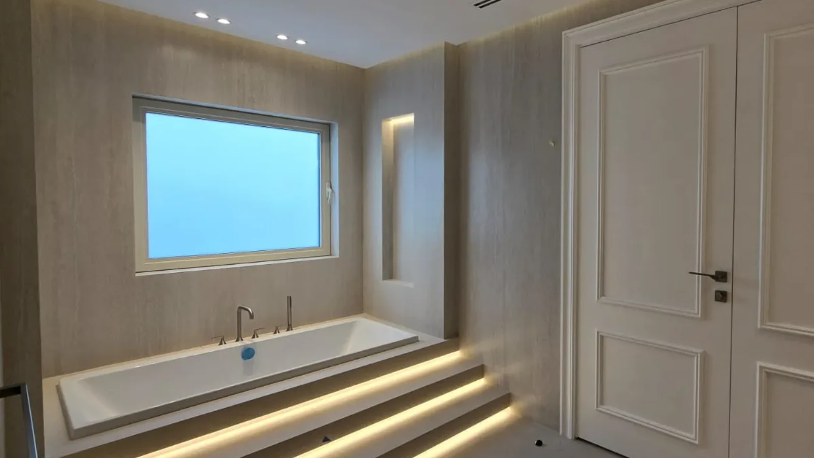 Master bathroom after renovation with rectangular bathtub, broad frosted window and illuminated stepped platform