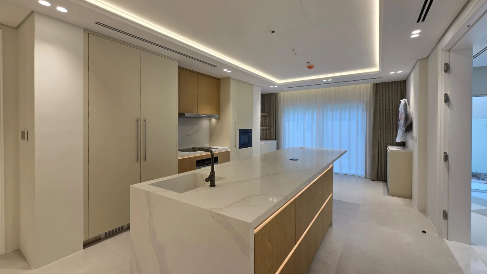 Completed Meadows villa kitchen with long stone island, pale cabinetry and oak joinery