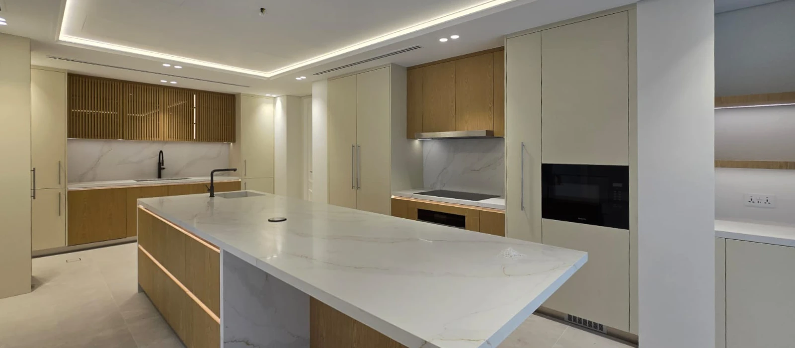 Completed kitchen renovation in The Meadows Dubai with long white stone island, oak cabinetry and full-height storage