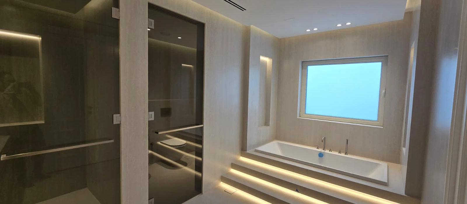 Renovated master bathroom in The Meadows Dubai with rectangular bathtub, smoked glass enclosures and integrated lighting