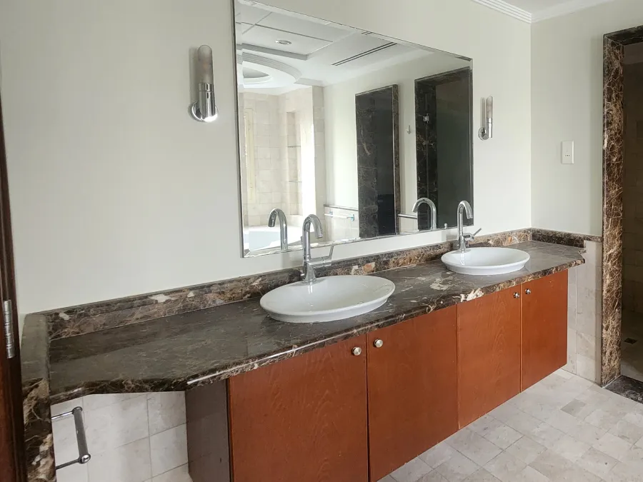 Original master bathroom vanity with dark stone countertop and reddish-brown floor standing cabinets