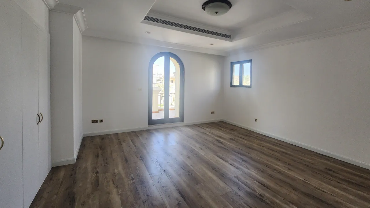 Palm Jumeirah guest bedroom before renovation with dark timber-look floor, arched balcony door and decorative tray ceiling