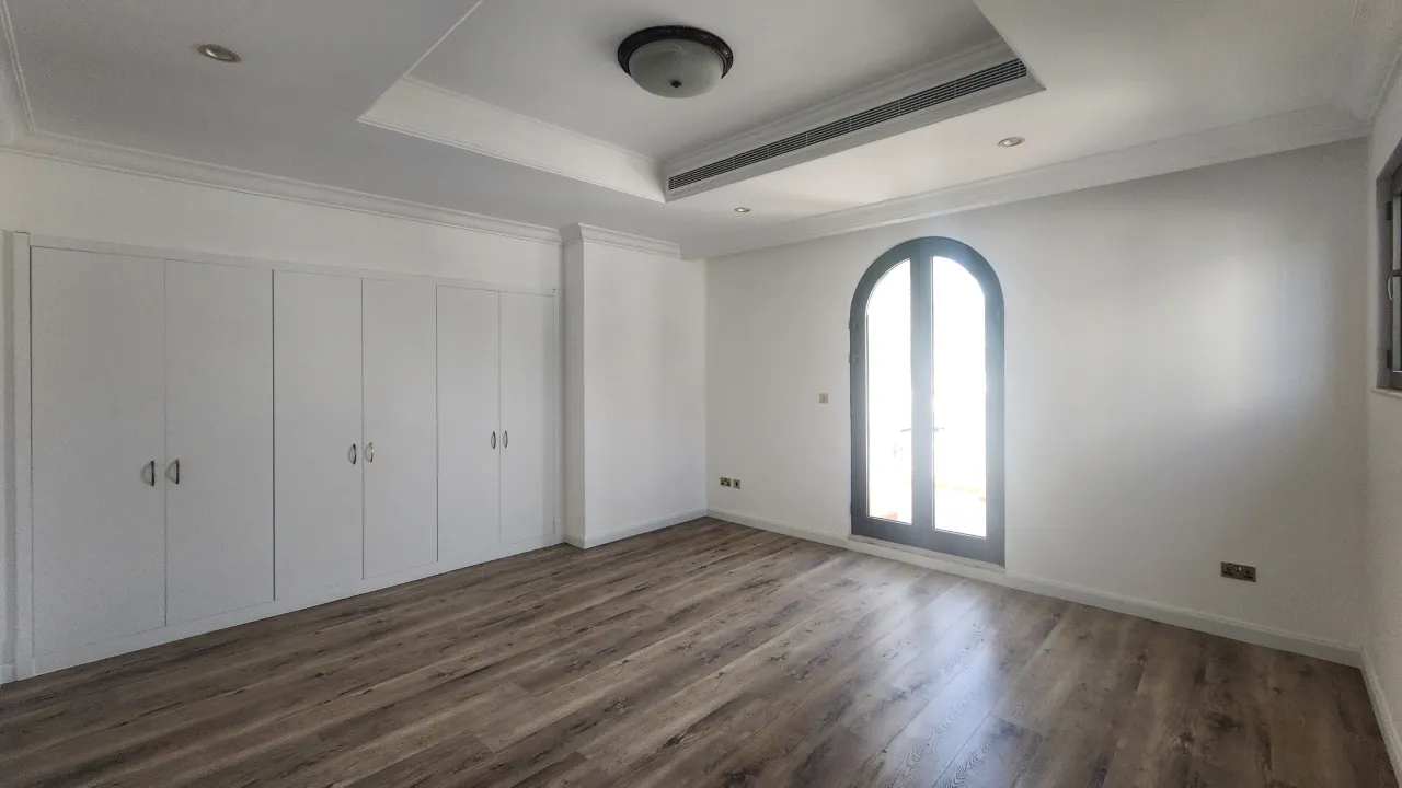 Palm Jumeirah guest bedroom before renovation with white panelled built-in wardrobes and dark flooring