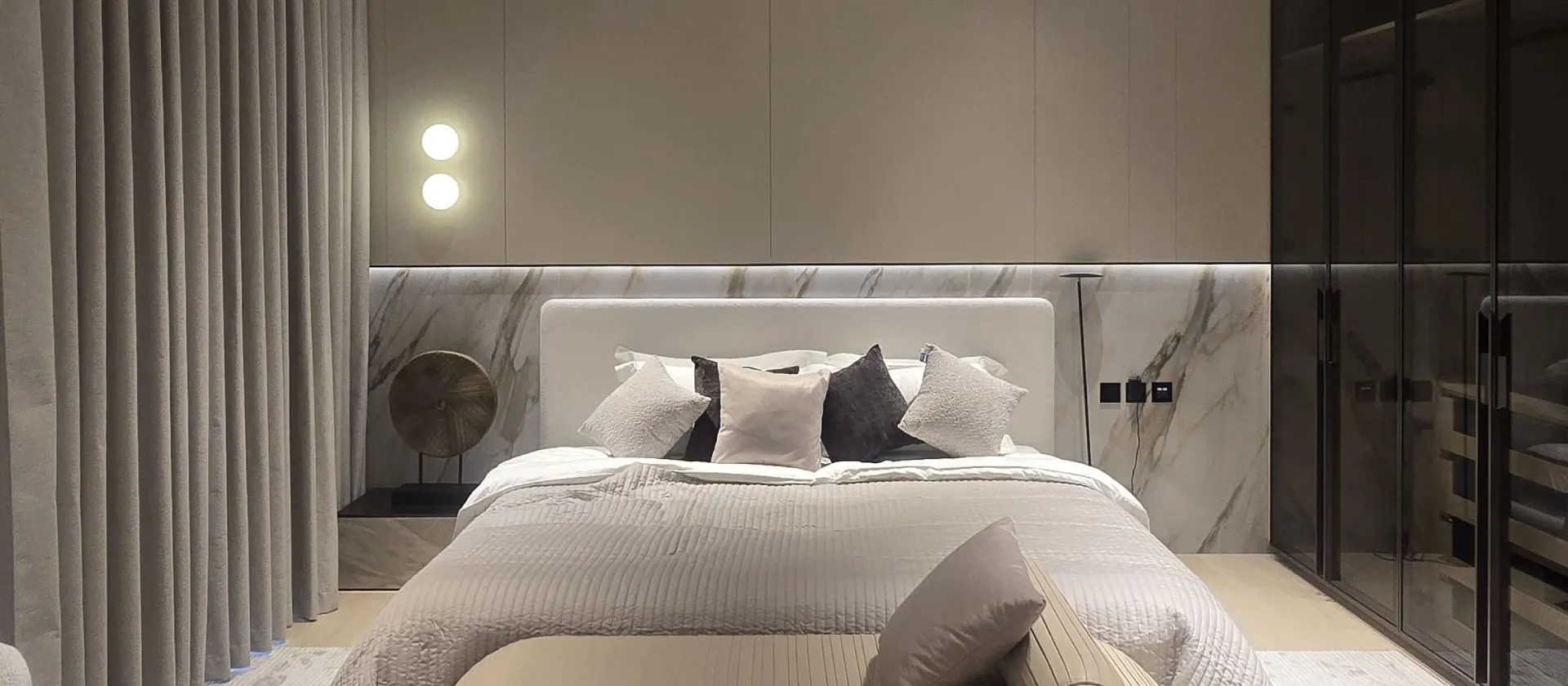 Completed Palm Jumeirah guest bedroom after renovation with upholstered bed, stone-effect headboard wall and smoked-glass wardrobes